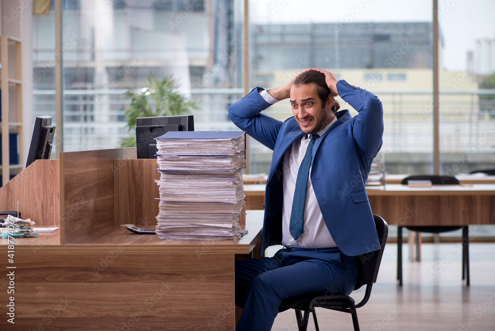 Young male employee unhappy with excessive work in the office Young male employee unhappy with excessive work in the office