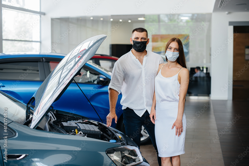 Young couple in masks selects a new vehicle and consult with a representative of the dealership in the period of the pandemic. Car sales, and life during the pandemic Young couple in masks selects a new vehicle and consult with a representative of the dealership in the period of the pandemic. Car sales, and life during the pandemic