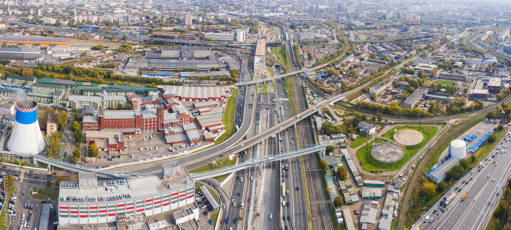 Power plant pipes and cooling towers in Moscow from above, automobile traffic and and construction of a new car overpass and interchange in the Moscow industrial zone near the automobile ring highway.