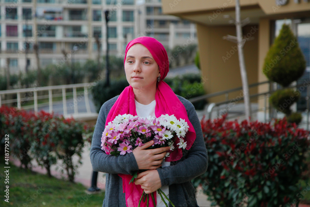 Fototapeta premium Girl in pink scarf and white mask with daisies outdoors. Cancer awareness concept. 