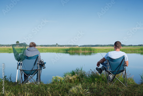 Two fisherman sits on the lake shore and fishing.