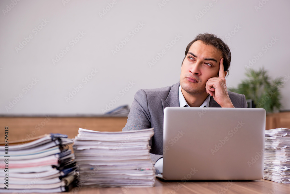 Young male employee unhappy with excessive work in the office Young male employee unhappy with excessive work in the office