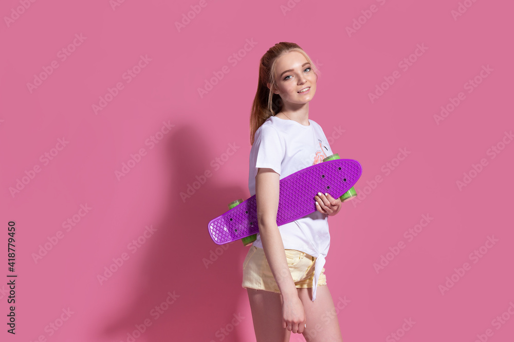 Cheerful young blonde girl with a skateboard on the pink background. Cheerful young blonde girl with a skateboard on the pink background.