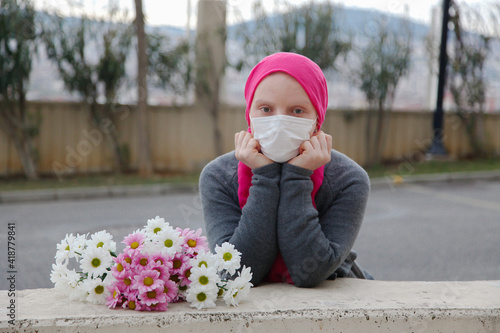 Girl in pink scarf and white mask with daisies outdoors. Cancer awareness concept. 