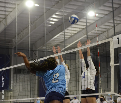 Female volleyball player hits the ball against a double block during a match