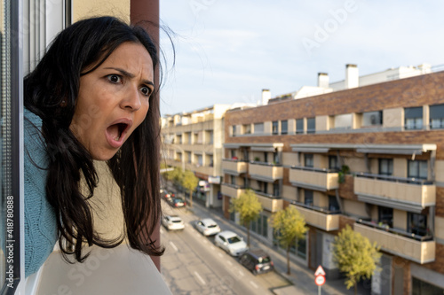 Adult woman looking out the window at home and putting surprise face.