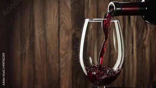 Wine. Red wine pouring from neck of bottle in wine glass over vintage wood background very close up view slow motion