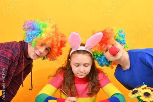 A girl is painting Easter eggs and two clown boys are looking around.