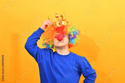 Fototapeta Naklejka Na Ścianę i Meble -  A boy with a clown wig straightens the crown on his head.