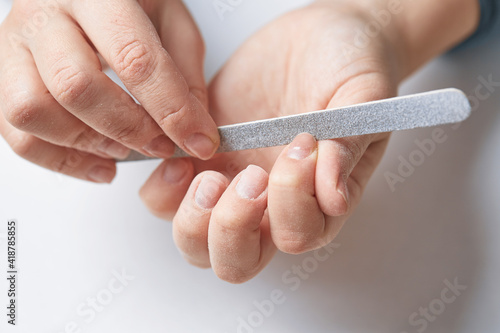 A woman does a manicure at home and uses a nail file to remove old gel polish from her nails. Close-up of a hand using a nail buffer when performing a manicure, polishing nails at home.
