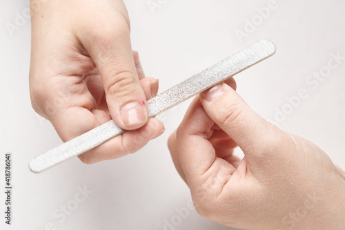 A woman does a manicure at home and uses a nail file to remove old gel polish from her nails. Close-up of a hand using a nail buffer when performing a manicure, polishing nails at home.