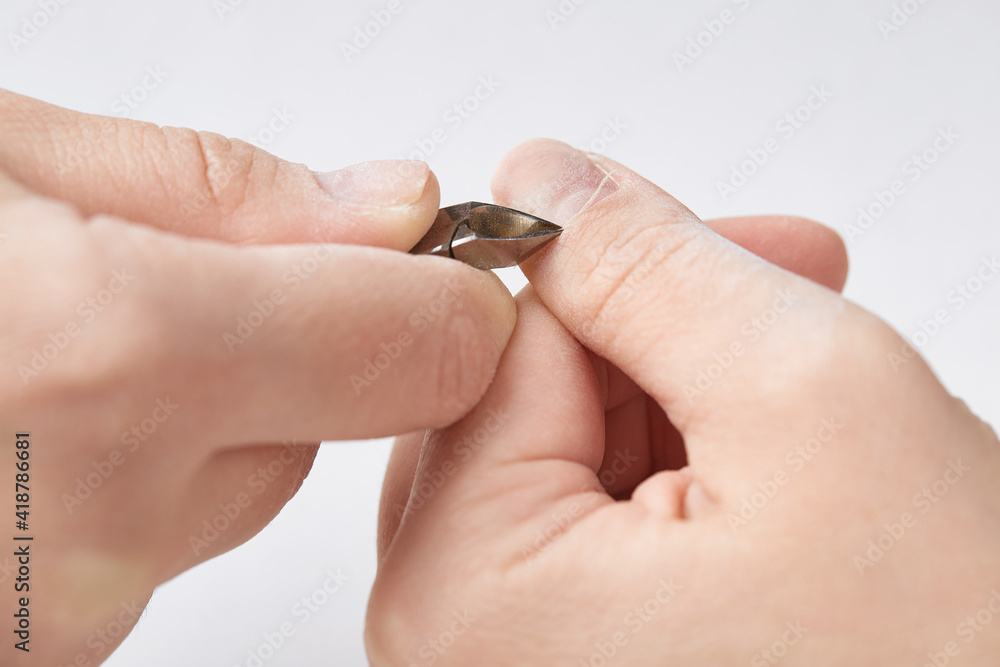 Treatment of the cuticle with forceps during the edged nail manicure. The girl makes herself an edged manicure at home. Cuticle treatment with forceps on a white isolated background. Close-up.