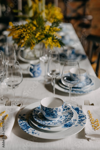 Table setting with vintage porcelain tableware, mimosa flowers and wine glasses.