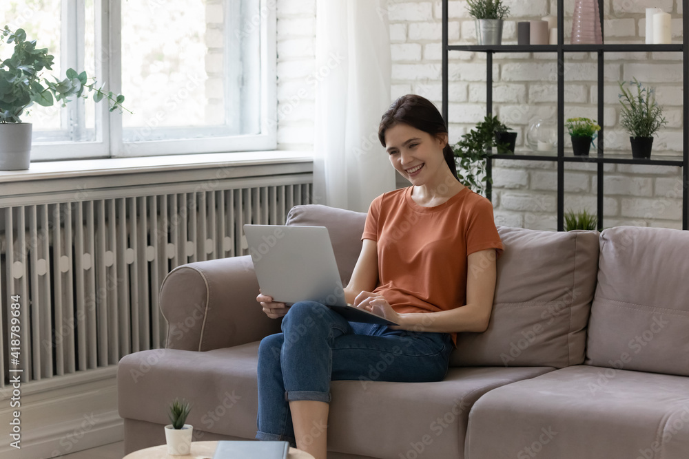 Leisure as pleasure. Happy young woman sit on couch at home relaxing on weekend with laptop chat with friends using wifi internet. Smiling teen female watching good movie online shopping browsing web Leisure as pleasure. Happy young woman sit on couch at home relaxing on weekend with laptop chat with friends using wifi internet. Smiling teen female watching good movie online shopping browsing web