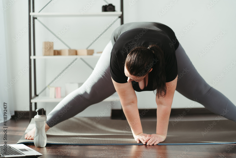 Fototapeta premium Home fitness, training online. Overweight woman looking tutorial video doing stretching exercise. Indoor yoga for home