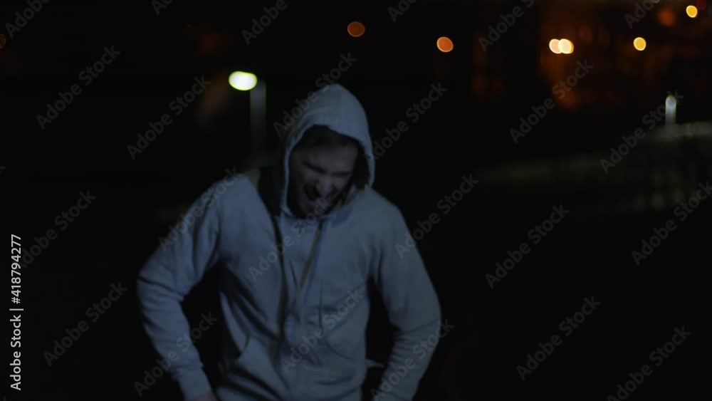 Young man stops for tiredness while running. Athlete trains outdoors at night. City lights, tired, running, evening