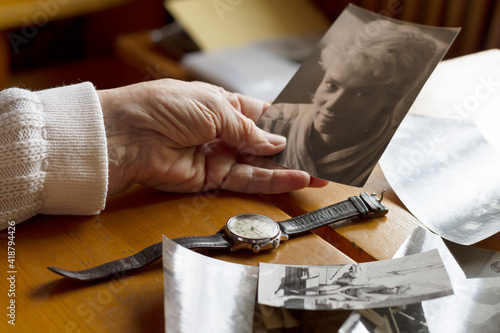 An old watch next to an old woman's hand. Next to old photos. Memories, nostalgia, time concept