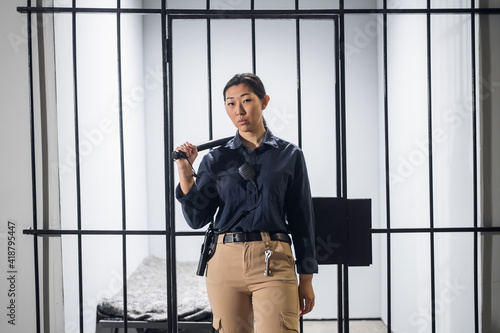 Canvas Print Asian guard in uniform In full armor with a baton and a pistol on the background of a prison cell