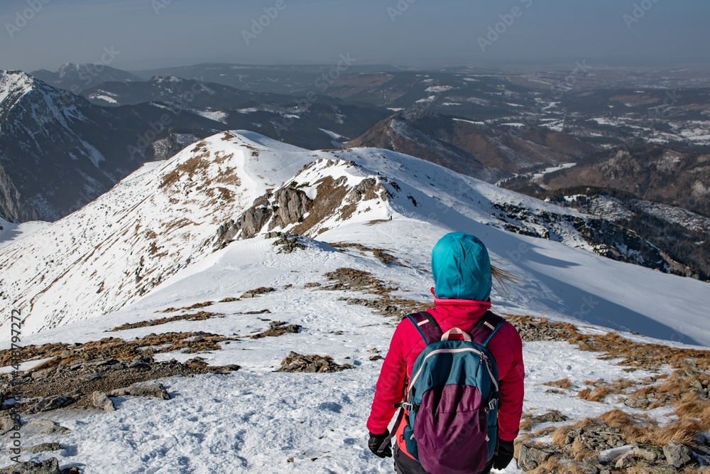 Female tourist in a hood with a backpack on a winter trail in the mountains.