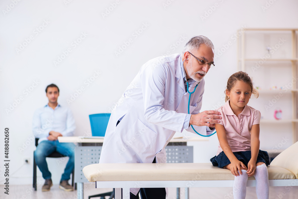 Fototapeta premium Small girl with her father visiting old male doctor