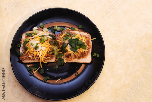 A delicious pulled chicken sandwich on a black plate. This sandwich is on white bread and contains pulled chicken, bbq sauce, cheddar cheese and green onions