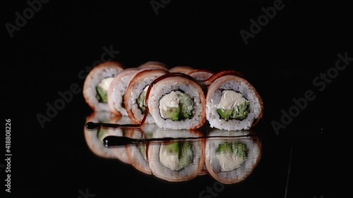 Chef's hands sprinkle sesame seeds on the inside out sushi. Japanese chef in black gloves at work preparing sushi roll with salmon and avocado.