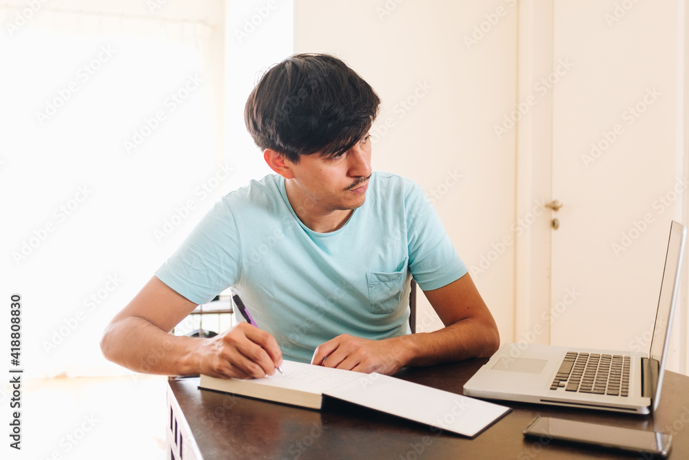 young man with laptop writing down in a notebook young man with laptop writing down in a notebook