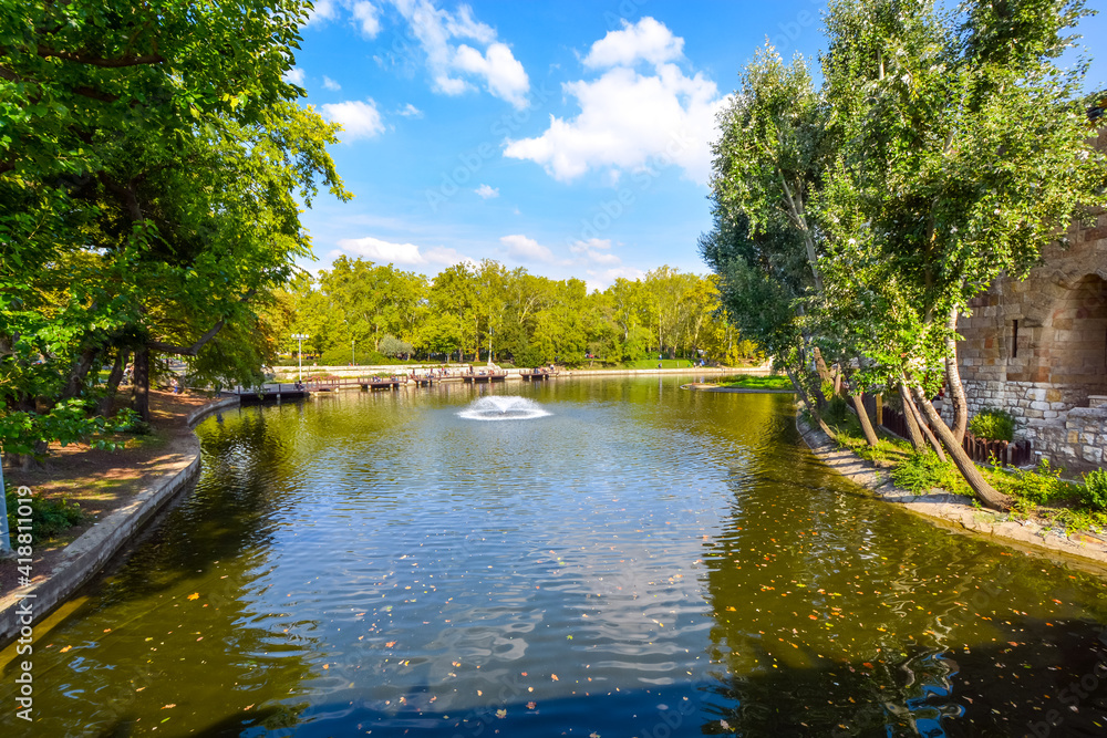 The small lake or moat surrounding Vajdahunyad Castle in the City Park of Budapest Hungary, with the castle visible on the right and a fountain in the middle. The small lake or moat surrounding Vajdahunyad Castle in the City Park of Budapest Hungary, with the castle visible on the right and a fountain in the middle.