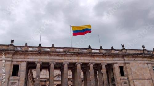 The flag of Colombia waves slowly on top of the House of Nariño (Casa de Nariño), the place where the president lives. The sky is cloudy and grey. photo