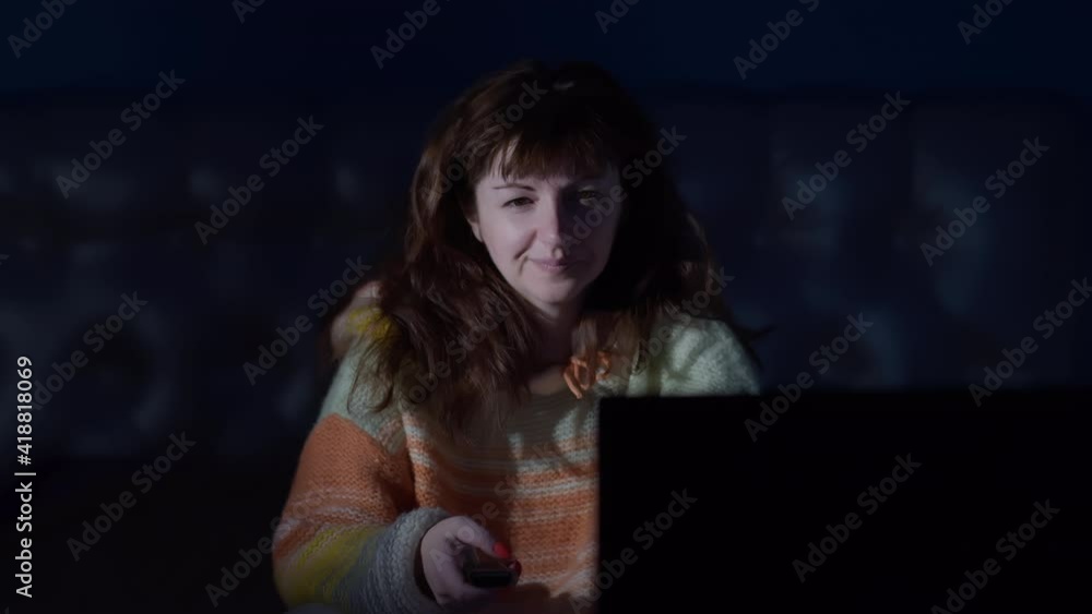 happy woman sitting on the bed at night and watches TV, switches channels and smiling happy woman sitting on the bed at night and watches TV, switches channels and smiling