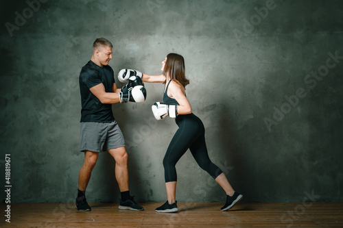 Young athletic COUPLE OF MAN AND WOMEN BOXING IN BOXING GLOVES. A WOMAN makes a blow to the head of a man on a dark gray background. Full length.