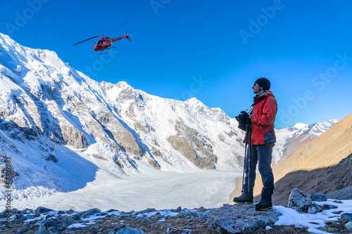 Beautiful landscape with mountains, a huge blue glacier and a silhouette of a man photographing a beautiful view against the background of mountains, a glacier and an ambulance helicopter