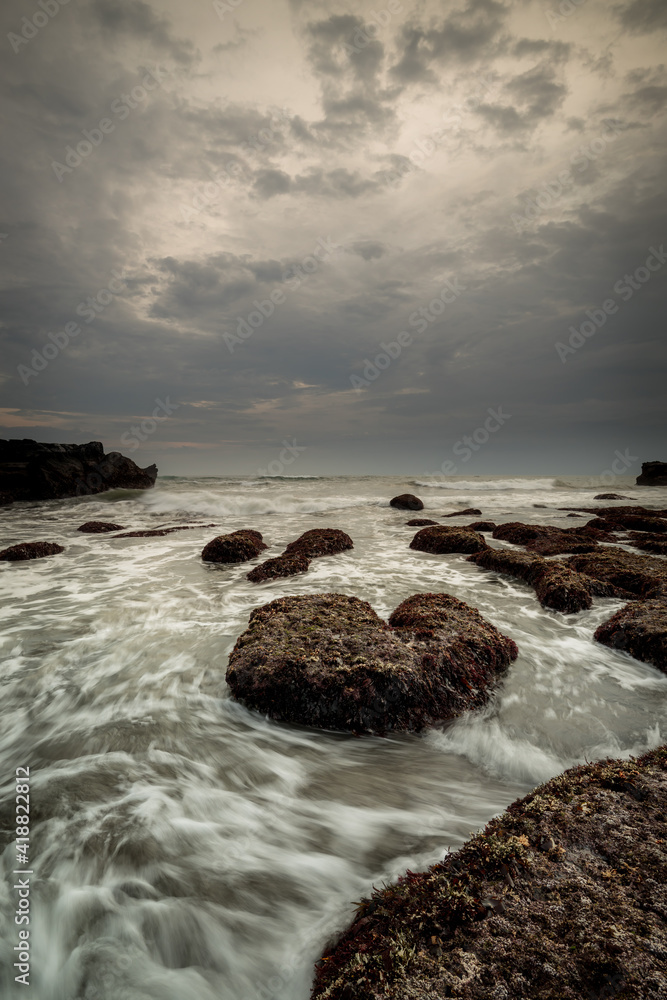 Beautiful seascape for background. Beach with rocks and stones. Low tide. Motion water. Cloudy sky. Slow shutter speed. Soft focus. Copy space. Vertical layout. Mengening beach, Bali