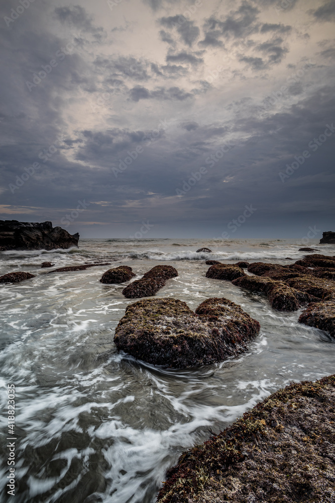 Beautiful seascape for background. Beach with rocks and stones. Low tide. Motion water. Cloudy sky. Slow shutter speed. Soft focus. Copy space. Vertical layout. Mengening beach, Bali