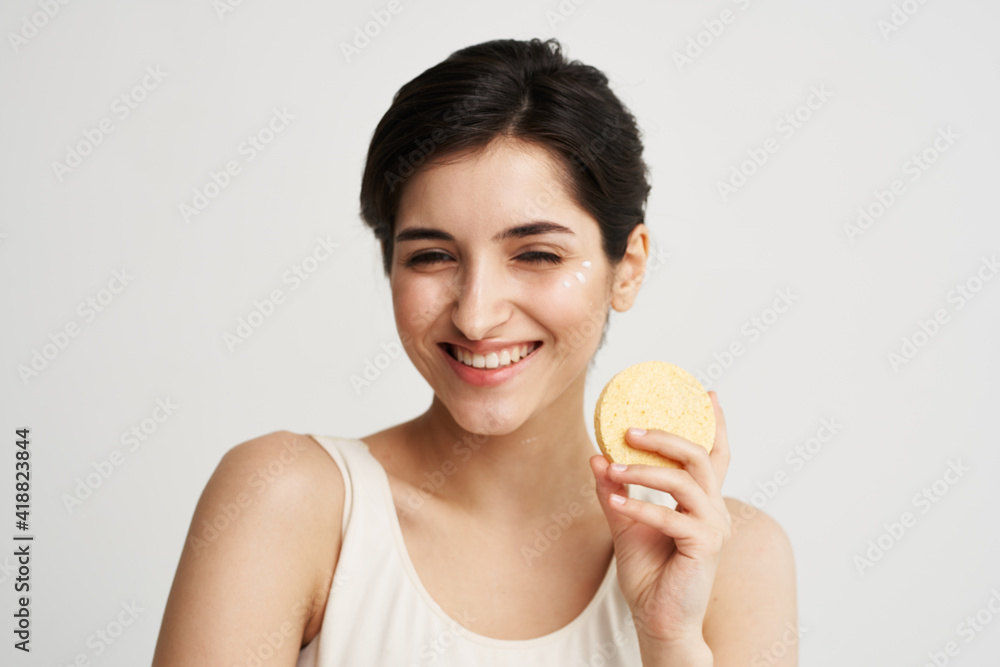 Cheerful pretty woman with a sponge in her hands skin care cosmetics color background light background Cheerful pretty woman with a sponge in her hands skin care cosmetics color background light background