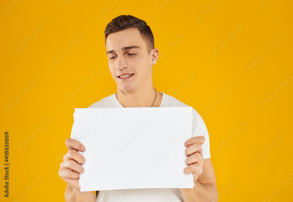 A man in a white T-shirt with a sheet of paper on a yellow background Copy Space mockup A man in a white T-shirt with a sheet of paper on a yellow background Copy Space mockup