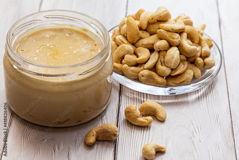 A jar of cashew butter with a bunch of fresh cashew on a white wooden table. Homemade cashew butter, natural, healthy food. The modern wellness and vegan concept. A jar of cashew butter with a bunch of fresh cashew on a white wooden table. Homemade cashew butter, natural, healthy food. The modern wellness and vegan concept.