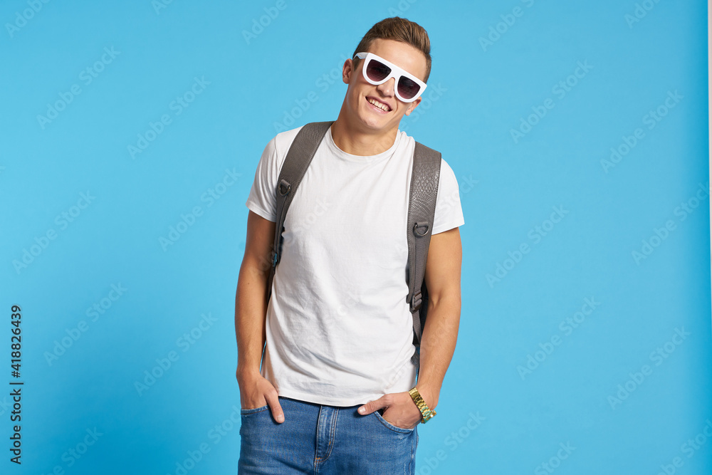 Relaxed guy in jeans with torn knees sits on a chair indoors on a blue background with full-length glasses on his face Relaxed guy in jeans with torn knees sits on a chair indoors on a blue background with full-length glasses on his face