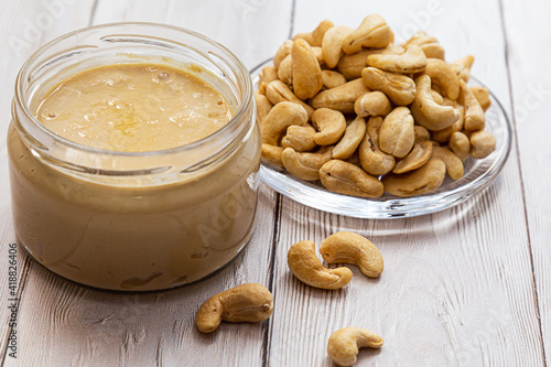 A jar of cashew butter with a bunch of fresh cashew on a white wooden table. Homemade cashew butter, natural, healthy food. The modern wellness and vegan concept.