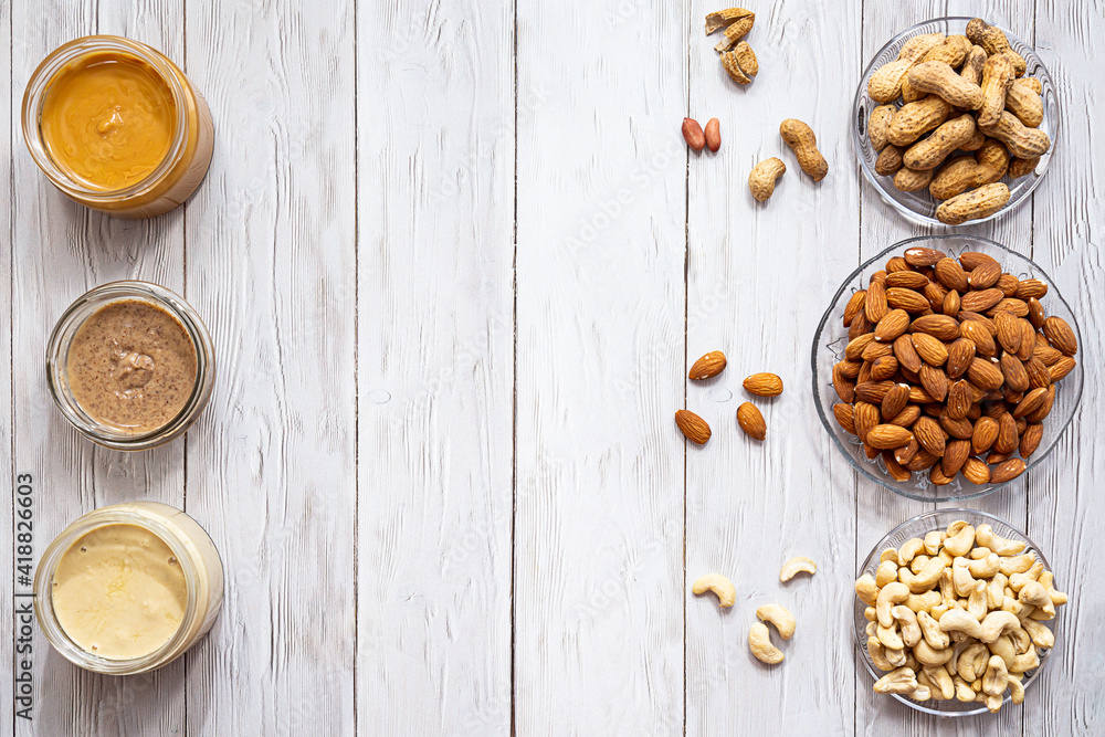 The modern concept of wellness and veganism. Jars of almond, cashew and peanut butter on a white wooden table. Organic, homemade nut butter for a healthy breakfast. The modern concept of wellness and veganism. Jars of almond, cashew and peanut butter on a white wooden table. Organic, homemade nut butter for a healthy breakfast.