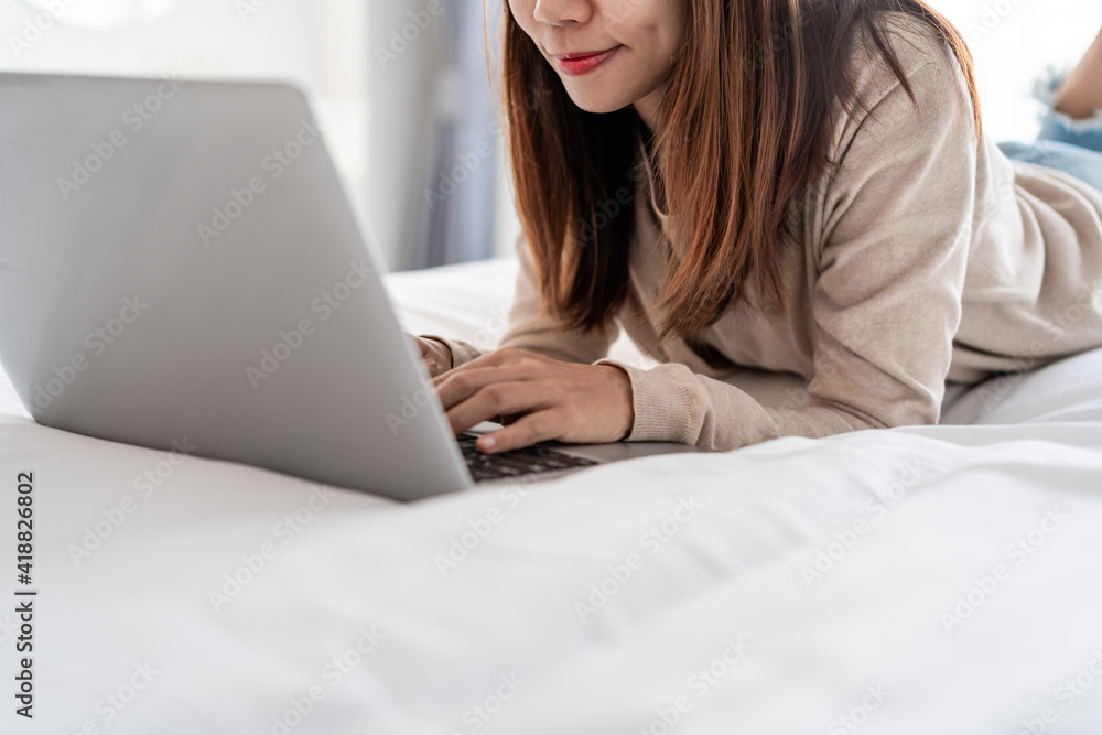 Young woman lying on bed at bedroom and using laptop at home Young woman lying on bed at bedroom and using laptop at home