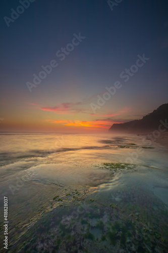 Seascape for background. Sunset time. Beach with rocks and stones. Low tide. Stones with green seaweed and moss. Blue sky with motion clouds. Copy space. Melasti beach  Bali