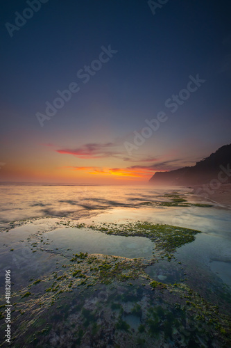 Seascape for background. Sunset time. Beach with rocks and stones. Low tide. Stones with green seaweed and moss. Blue sky with motion clouds. Copy space. Melasti beach  Bali