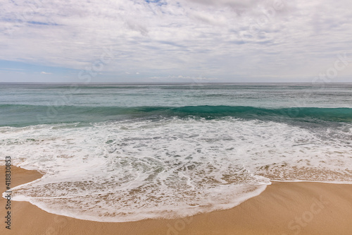 Seascape background. Sandy beach  milky foam waves  blue ocean. Scenic waterscape. Horizon line. Cloudy sky. Nature and environment concept. Daylight. Copy space. Dreamland beach  Bali