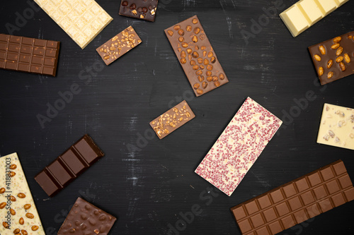 a lot of different sweet, delicate chocolate bars lie creatively on a black wooden background