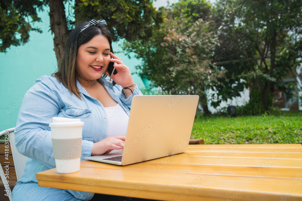 Plus size woman talking on the phone and using laptop.