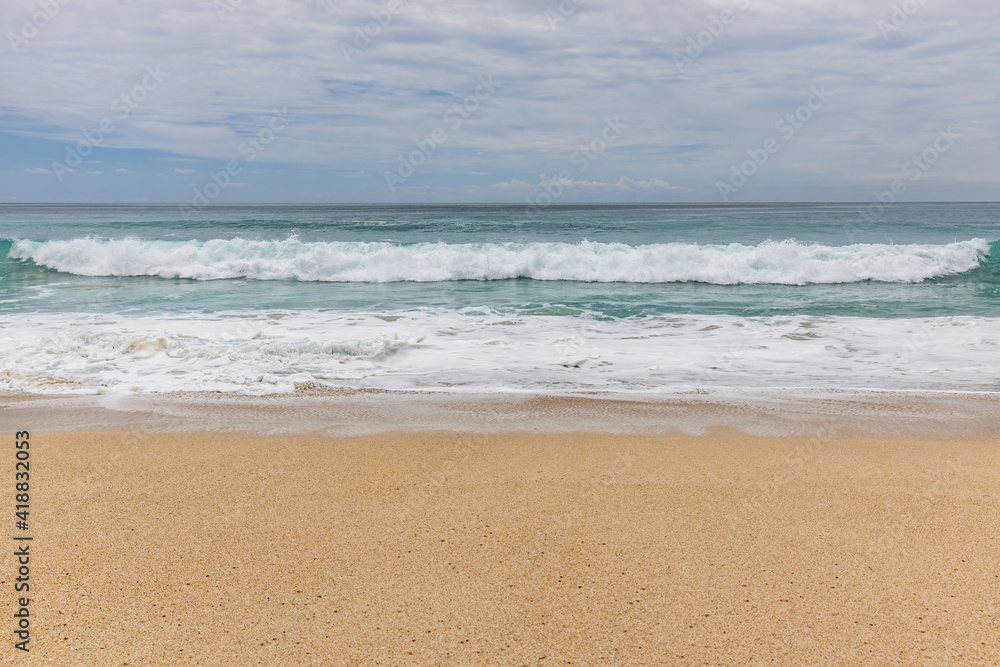 Seascape background. Sandy beach, milky foam waves, blue ocean. Scenic waterscape. Horizon line. Cloudy sky. Nature and environment concept. Daylight. Copy space. Dreamland beach, Bali