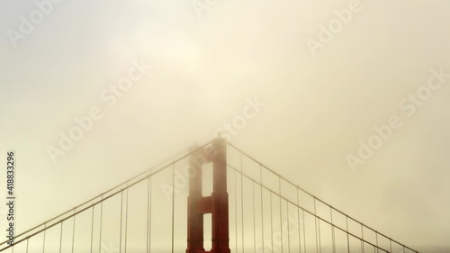 Aerial shot of Golden Gate Bridge under foggy weather, drone flying by famous landmark - San Francisco, California
