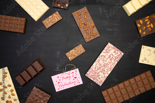 a lot of different sweet, delicate chocolate bars are creative on a black wooden background with a label that says happy valentine with a vintage cord