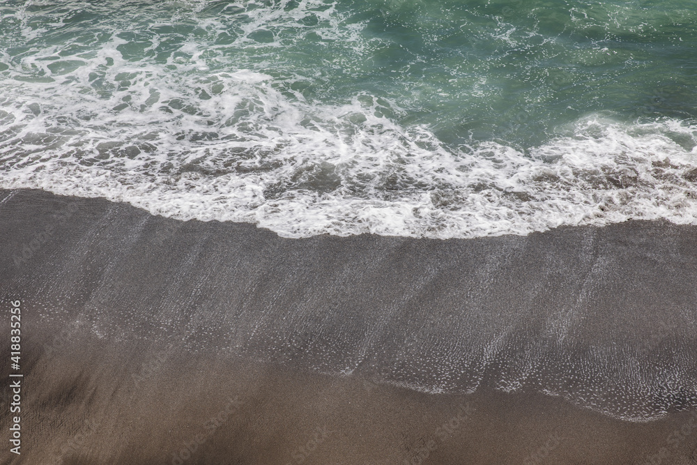 Waterscape background. Black sand beach with white milky foam waves. Nature and environment concept. Black and white contrast. Daylight. Copy space. Volcanic beach in Bali